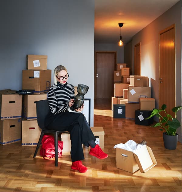 빈방에 이삿짐을 정리하는 여자, 그리고 다양한 이사용품과 JÄTTENE 예테네 상자가 쌓여 있습니다.