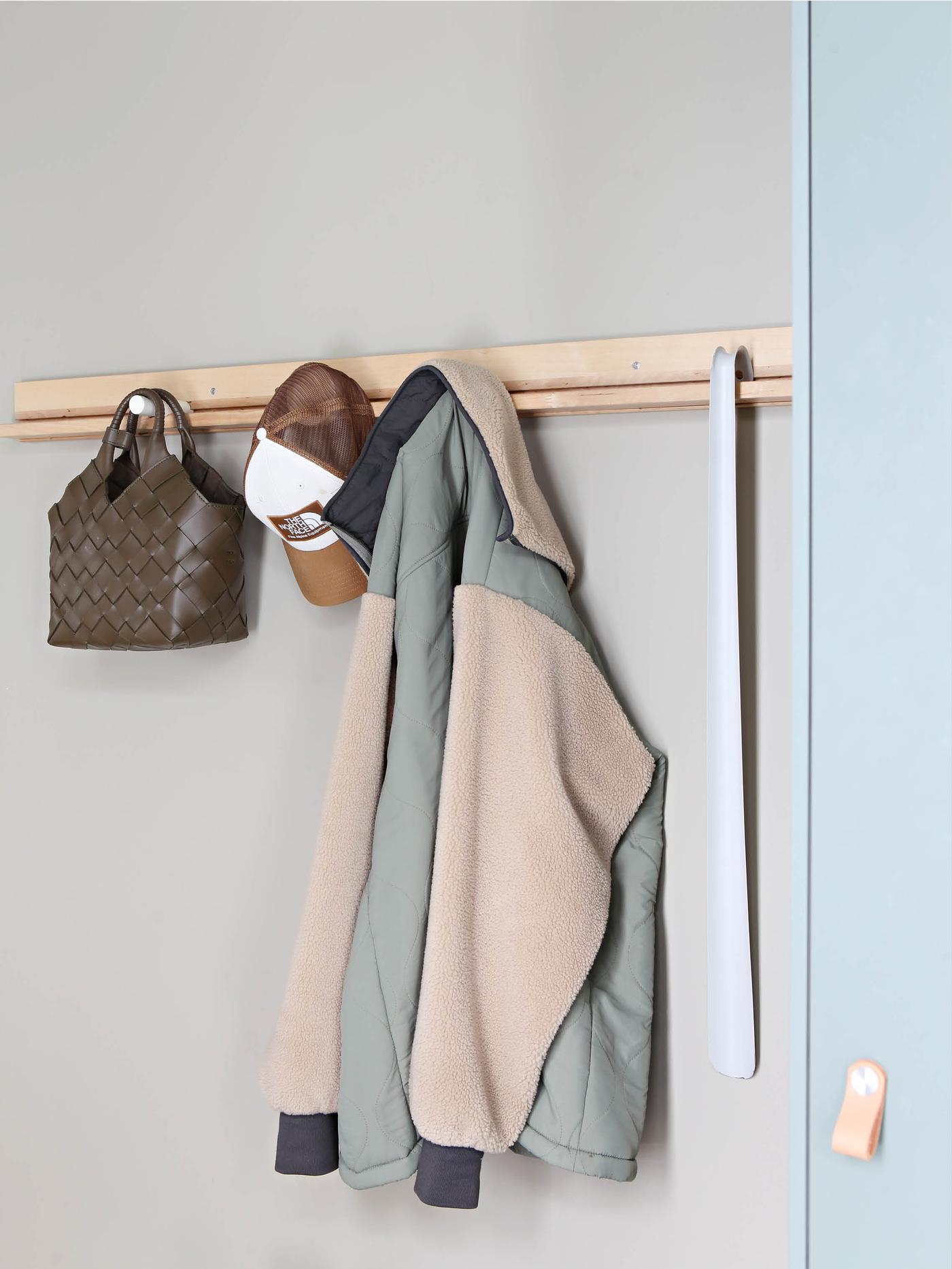 Jakke og veske henger på knagger i en gang.