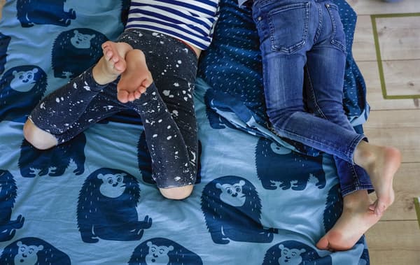 Jambes de deux garçons couchés sur un lit revêtu d’une couette bleue décorée de motifs d’animaux.