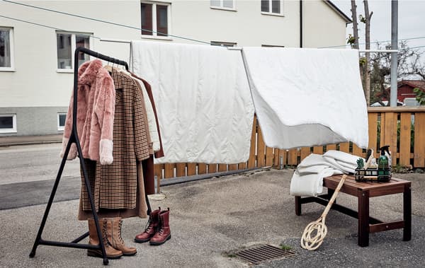 Jardim da frente pavimentado, preparado para uma limpeza de primavera: edredões pendurados em cordas, um suporte para cabides, calçado, têxteis e acessórios de limpeza.
