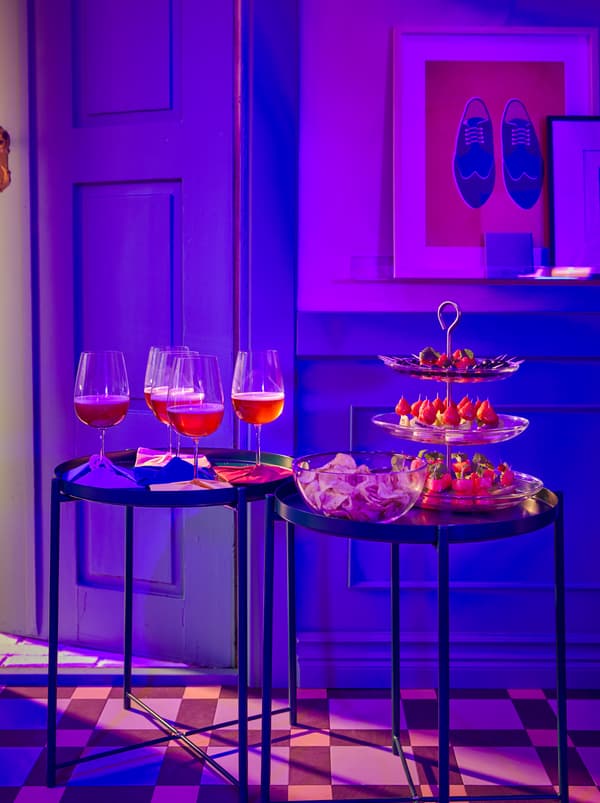Járólapos előszoba, lila színben, üdvözlő falatokkal egy KVITTERA tálalóállványon és italokkal STORSINT borospoharakban.