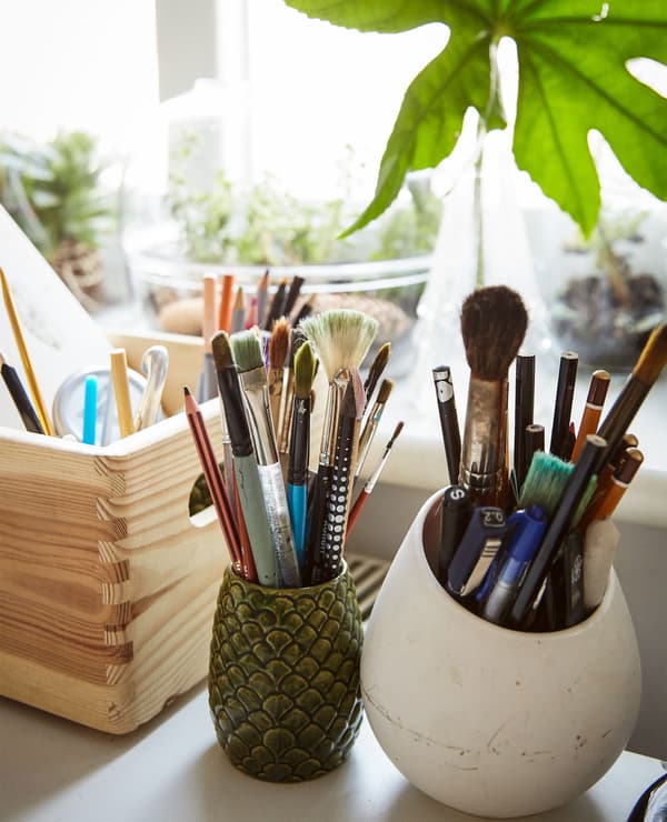 Jars and a wooden box filled with artist's brushes and pens.