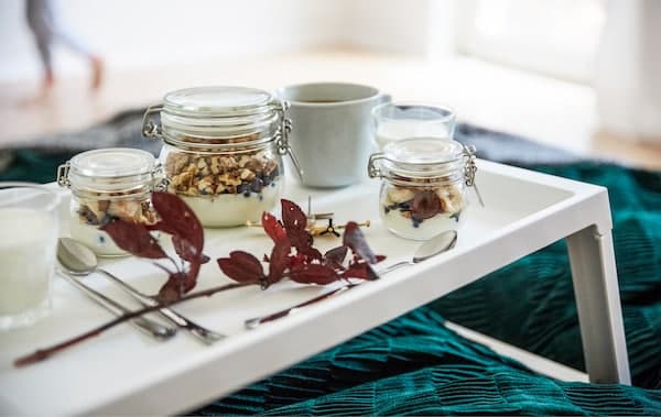 Jars filled with granola and yoghurt on a white tray on a bed.