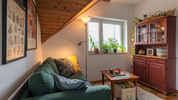 Jasny pokj dzienny z drewnianymi skosami, dużym oknem i drewnianym kredensem.