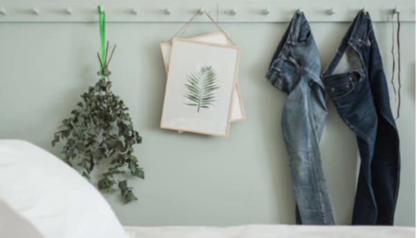 Jeans, dried plants and artwork hanging on hook racks painted the same light green colour as the bedroom wall 