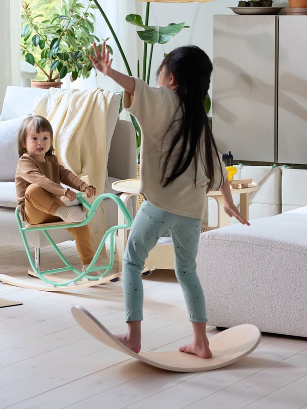 Jedno děvčátko udržuje rovnováhu na balanční desce GREJSIMOJS, druhé se houpá na houpacím ptáčku GREJSIMOJS.