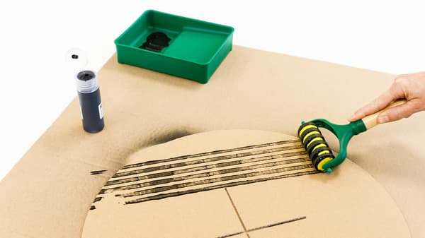 Jemand zieht mit einem Roller Striche auf der Kartonplatte.