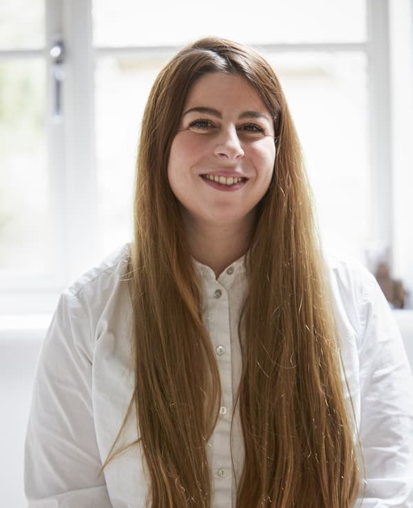 Jeune femme aux cheveux longs et roux portant un chemisier blanc.