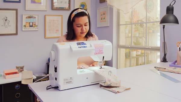 Jeune femme cousant à la machine, assise dans une pièce bien rangée.