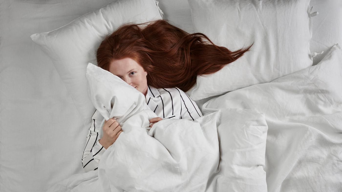 jeune femme en pyjamas rayé dans un lit avec textiles blancs