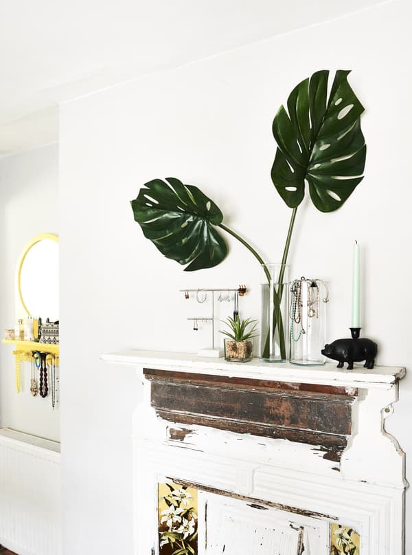 Jewellery and plants displayed on a fireplace mantle in a white room.