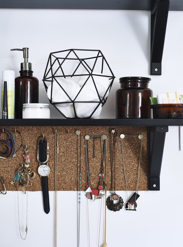 Jewellery hanging from a cork board below a shelf.