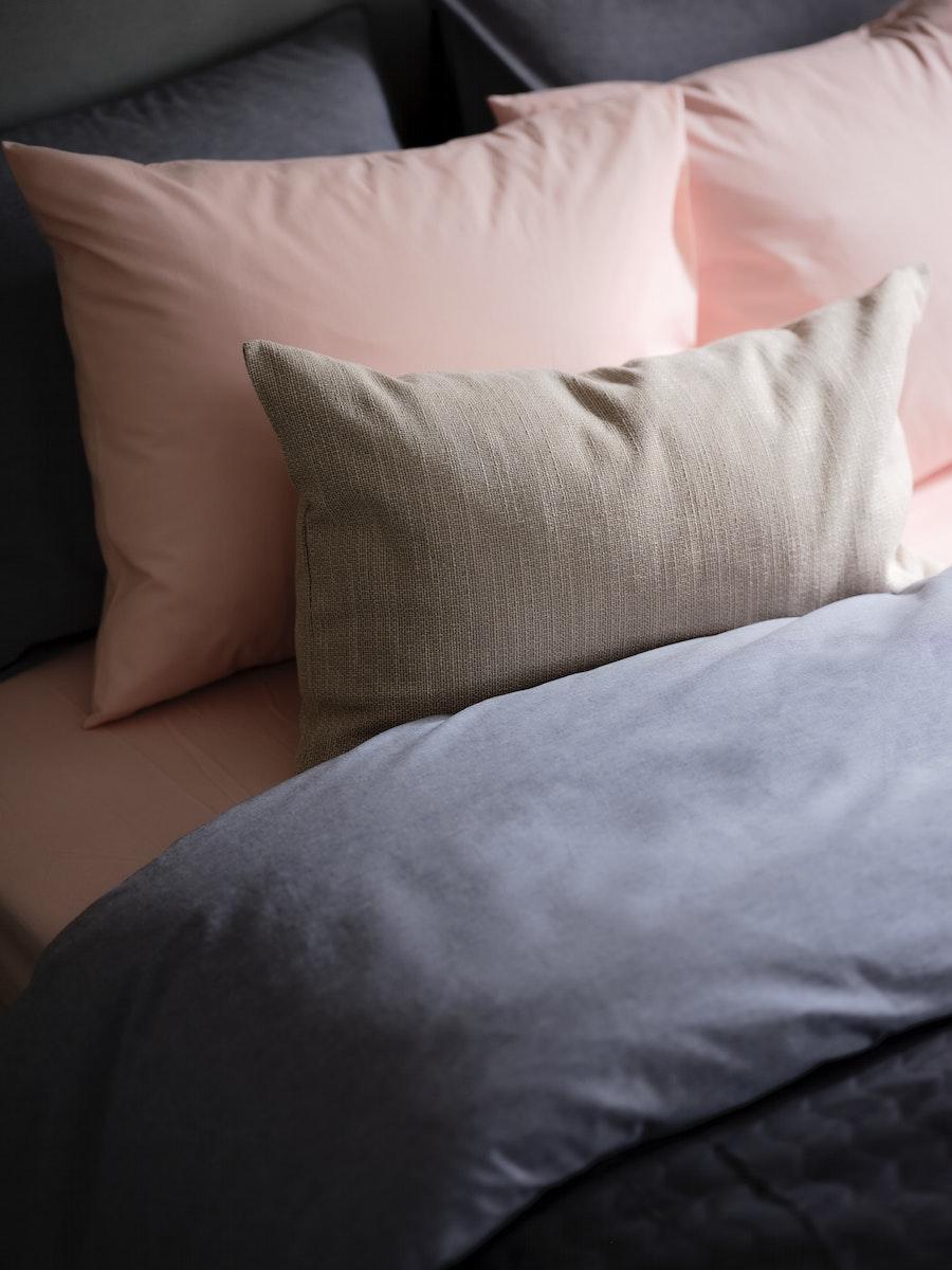 Juego de sábanas DVALA : Una rasa de base y una azul superior. Se ven también almohadas con la funda de las sábanas rosa y gris