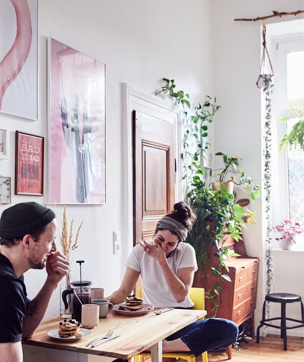 Julia et André devant leur petit déjeuner sur une table à rabat avec des plantes et des œuvres d’art aux murs.