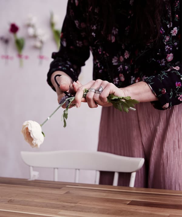 Julia taille une rose artificielle au-dessus d'une table en bois.