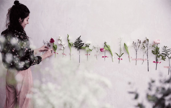Julia tapes single flower stems in a line along a white wall.
