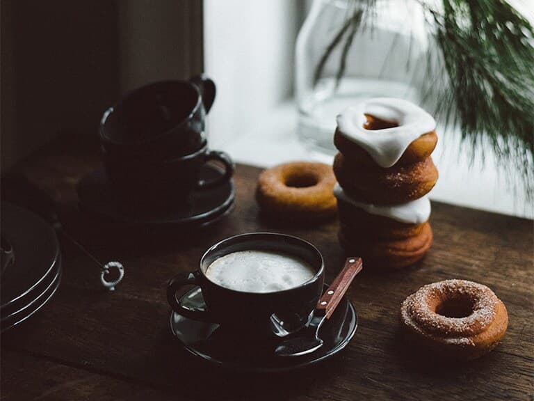 Juliga donuts ligger på ett rustikt bord bredvid svarta kaffekoppar och en av kopparna är fyllt med kaffe.