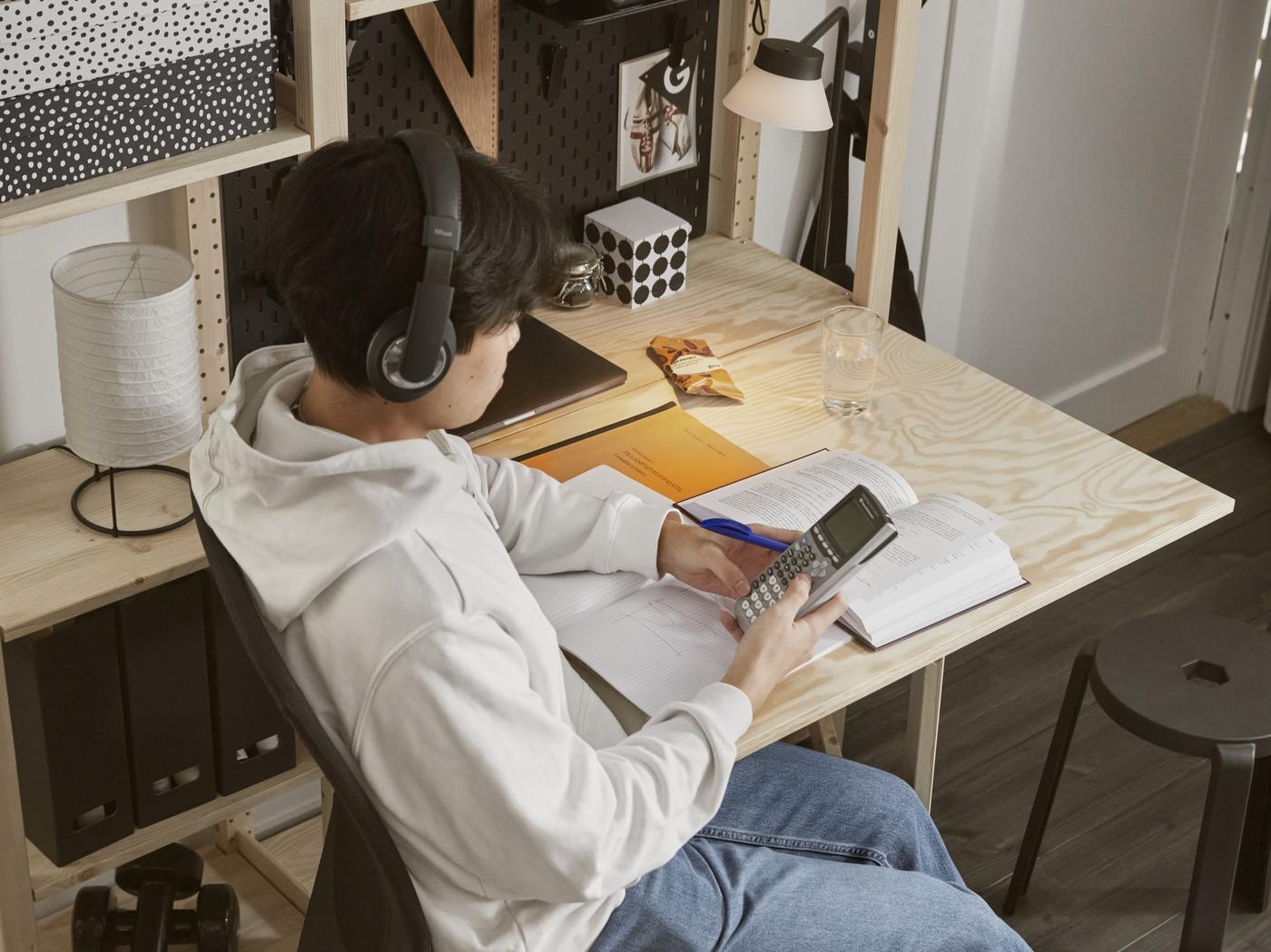 Junger Mann sitzt mit Kopfhörern am Schreibtisch und liest