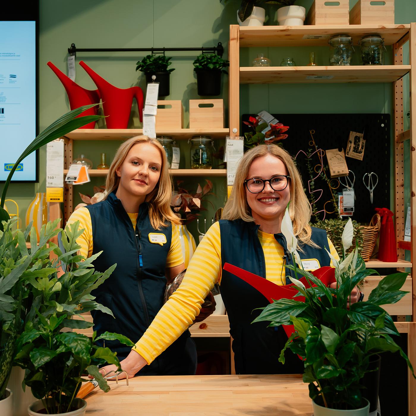 Kaks IKEA töötajat kollastes vormiriietes seisavad Tallinna poe lasteosakonnas riiulite ja väljapanekute kõrval; üks hoiab kätt mänguasjast ahvi ümber, taustal on laste mööbel ja ekraan tekstiga „LASTARE“.