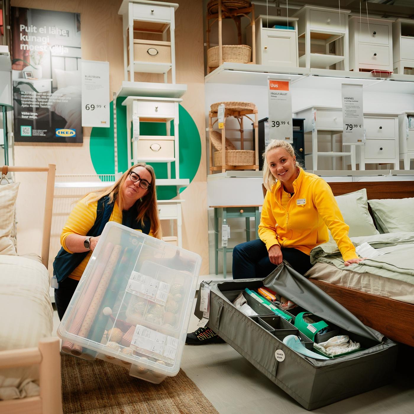 Kaks rõõmsameelset IKEA töötajat tutvustavad Tallinna poe näidistesaalis nutikaid hoiulahendusi, hoides käes erinevaid hoiukaste, mis sobivad hästi voodialuseks panipaigaks.