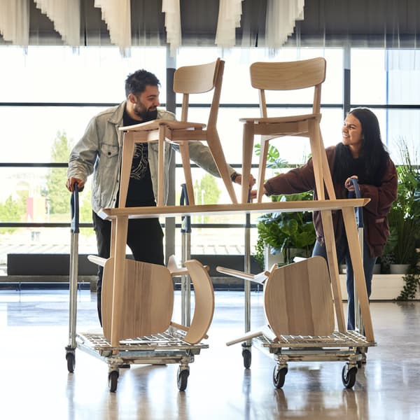 Kaksi henkilöä työntää tuoleilla täytettyä kärryä IKEA-tavaratalon aulassa.