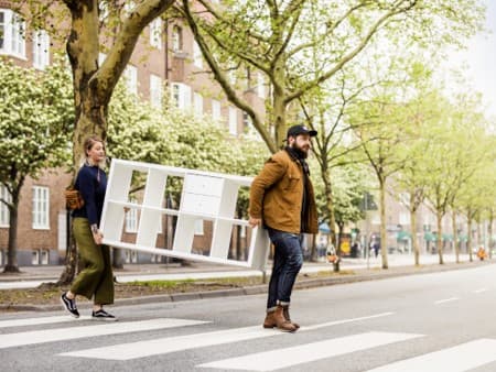 Kaksi ihmistä kantamassa valkoista lipastoa suojatien yli