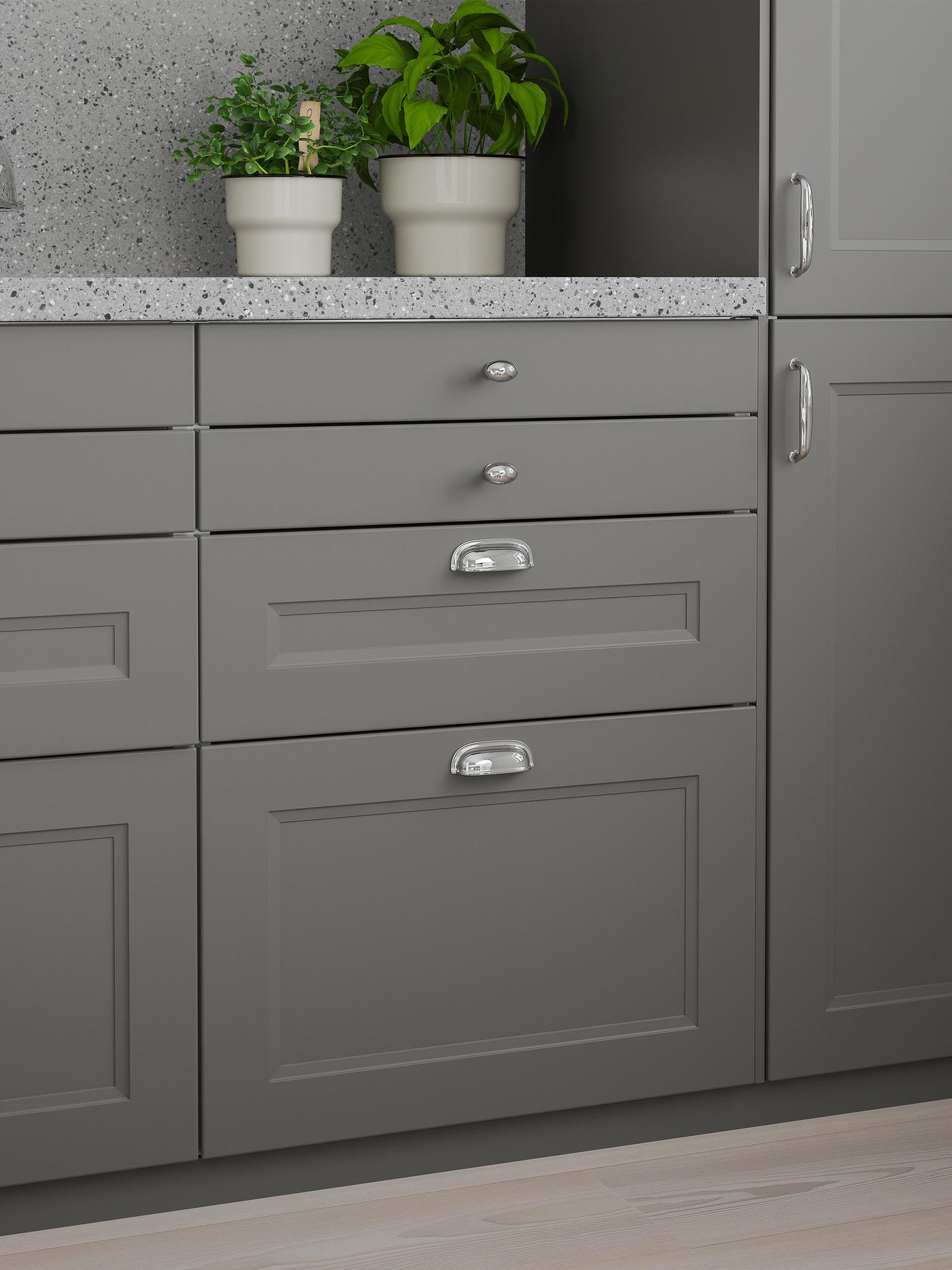Kaksi keittiökaappia, joissa on tummanharmaat ovet, tummanharmaa kivinen työtaso, jonka päällä on kaksi lehtikasvia.