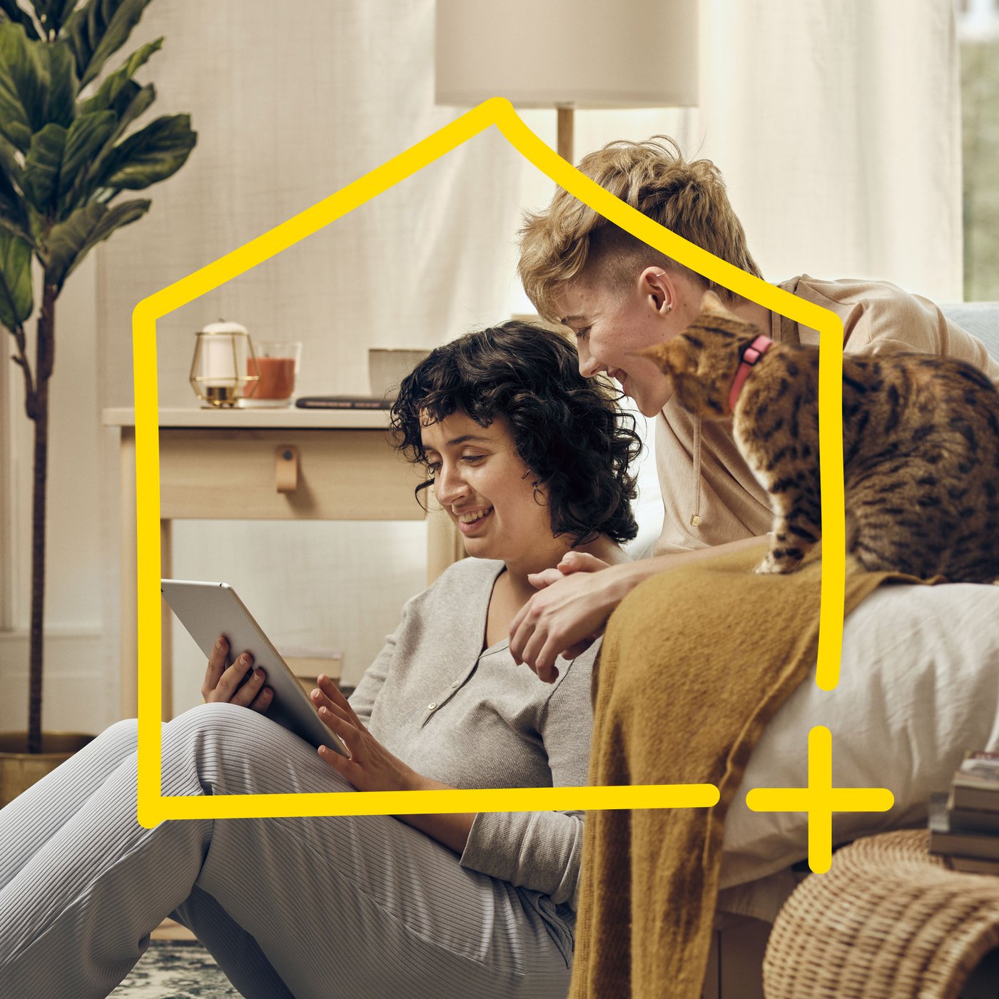 Kaksi naista ja kissa istuvat sohvalla ja katsovat tablettia.