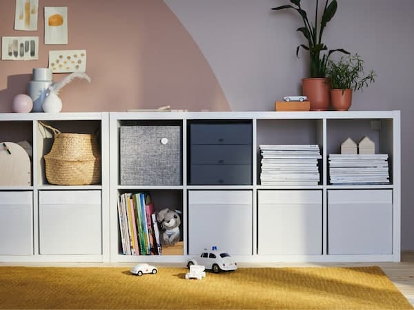 KALLAX Sideboard auf einem gelben Teppich vor einer rosafarbenen Wand.