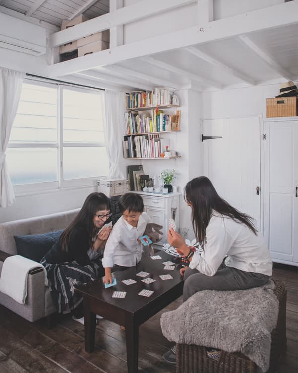 Kaoli, Shige and Tokiwa play card games at their black coffee table in the living room space of their small white home.