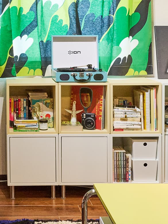 カラフルなカーテンの前に、レコードプレーヤーや本、雑貨が並ぶ棚。