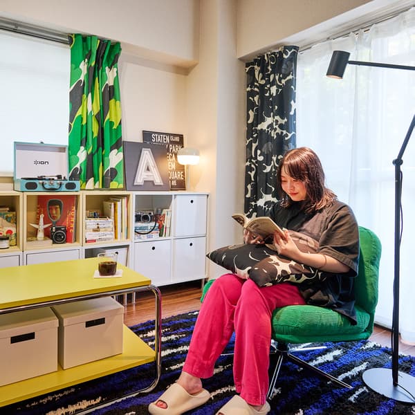 カラフルなカーテンと棚のある居心地の良い部屋で、緑の椅子に座って本を読む人物。