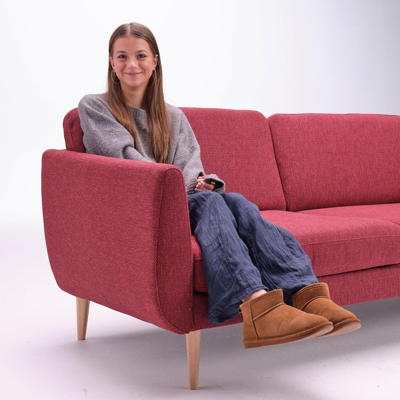 Karoline sidder i en sofa og smiler.