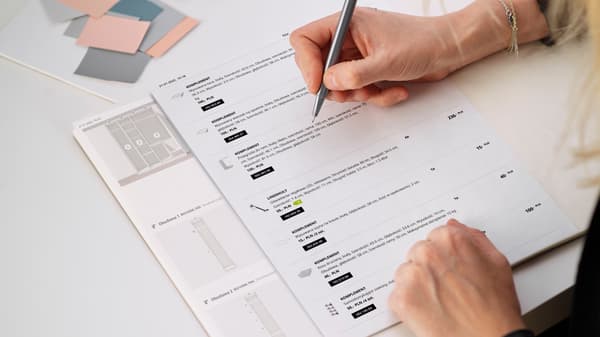 Kartki z wydrukiem projektu szafy PAX i listą zakupów, na których kobieta nanosi notatki.
