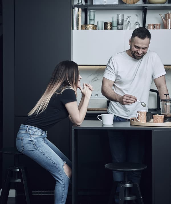 Katarzyna seduta su uno sgabello vicino all'isola per cucina nera dove Mikolaj prepara il caffè.