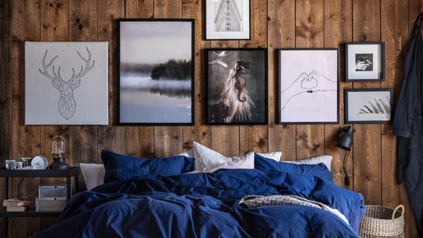 Katil dengan linen katil berwarna biru/putih di hadapan dinding kayu yang dihiaskan dengan pelbagai gambar dalam warna hitam, putih dan kelabu.