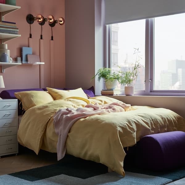 Katil sofa FLOTTEBO dengan sarung VISSLEBO berwarna ungu di dalam bilik kecil dengan kabinet storan, di tepi tingkap dengan tumbuh-tumbuhan di ambang tingkap.