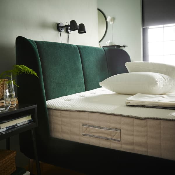 Katil upholsteri berwarna hijau, tilam berwarna putih/kuning air, dua bantal berwarna putih, linen katil yang dilipat dan dua lampu dinding berwarna hitam.