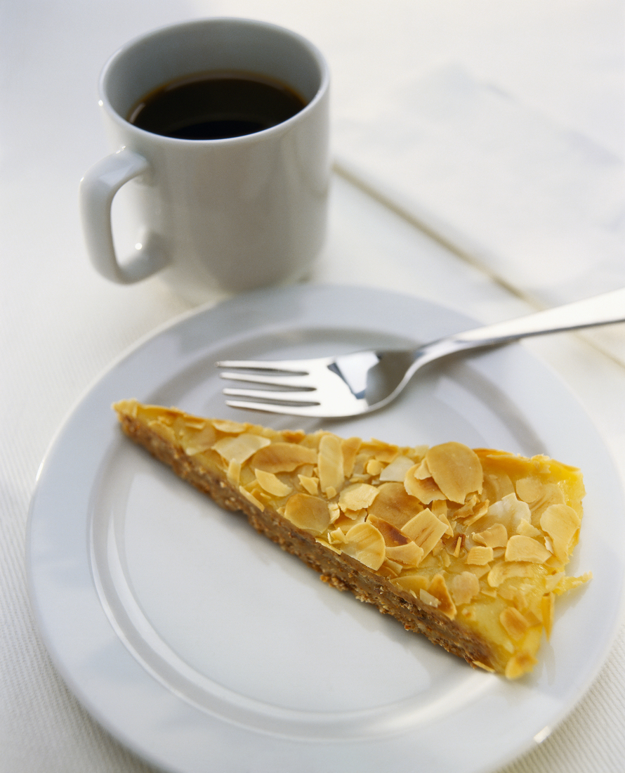 Káva v bílém hrníčku a madlový dortík na bílem talířku.