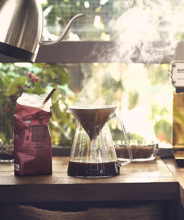 Kávéfőző készlet zöld háttér előtt: forró víz egy üvegkancsóban.