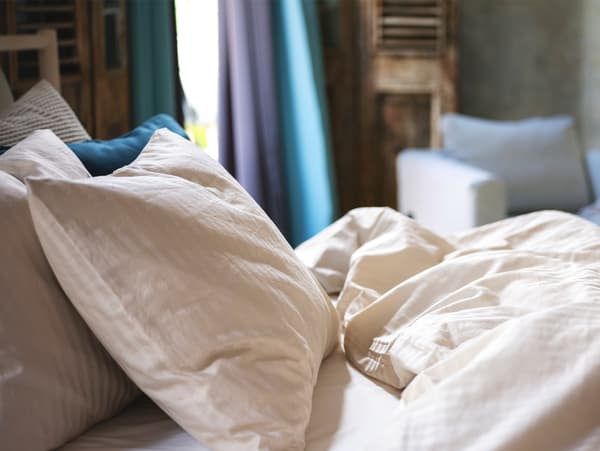 Kelengkapan tidur tenunan satin berwarna kuning air lembut terletak di atas katil dalam persekitaran bilik tidur.