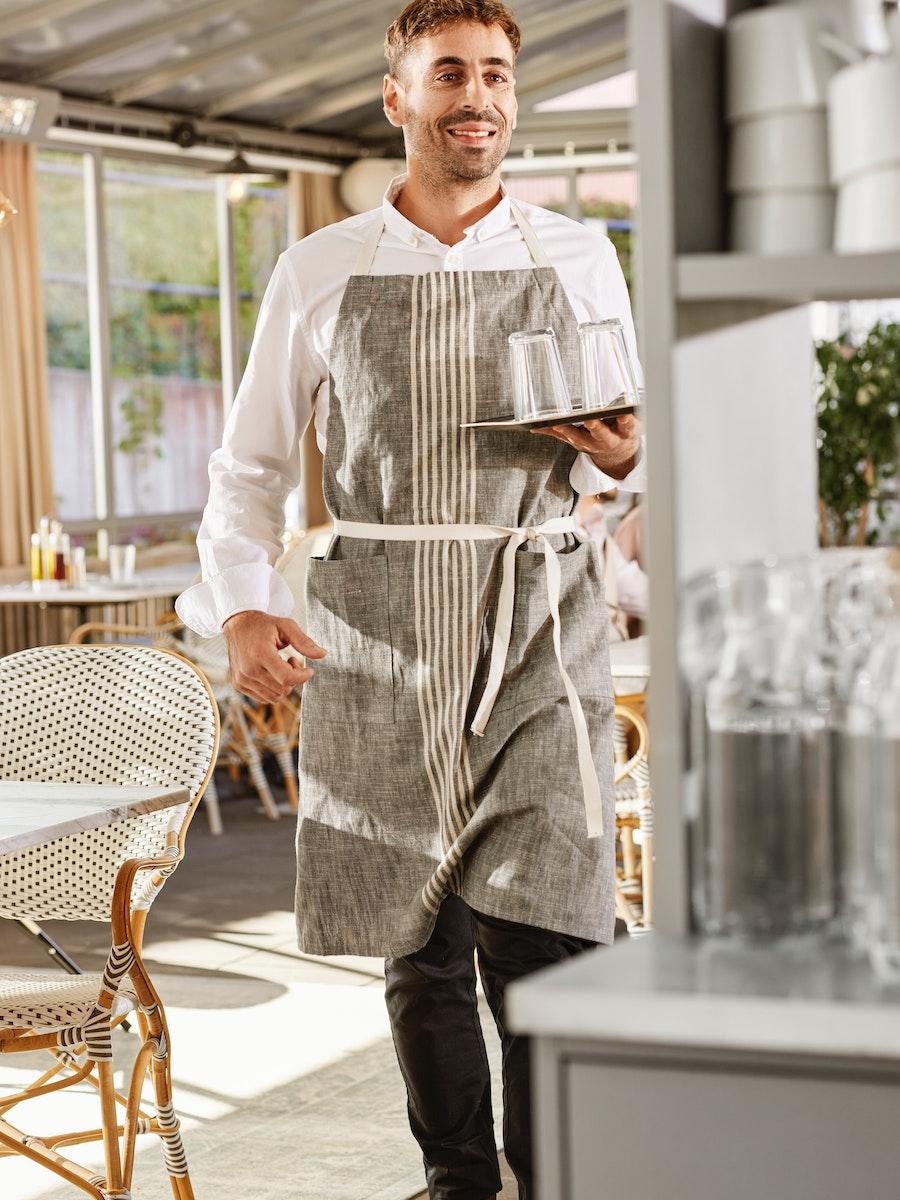 Kelner w fartuchu niosący tacę.