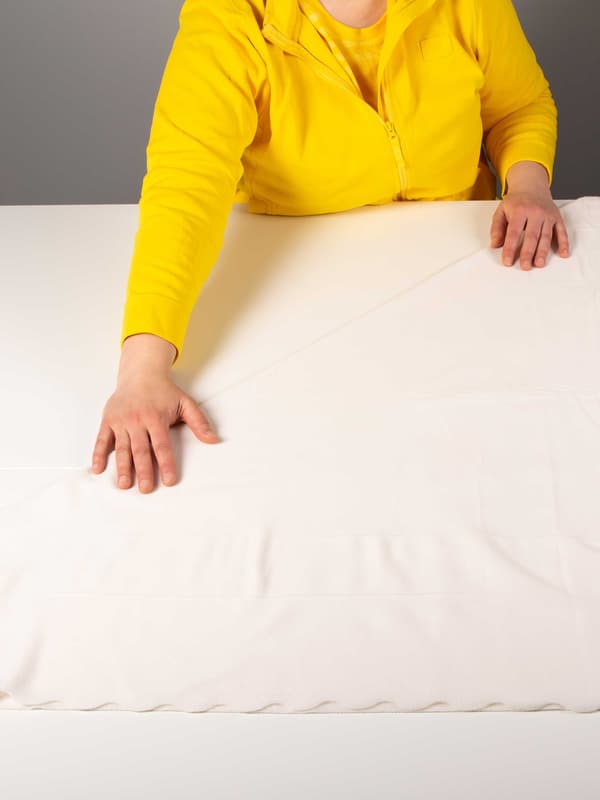 Keltaiseen IKEA-työntekijän asuun pukeutunut henkilö taittelee vaaleaa THORGUN-vilttiä.