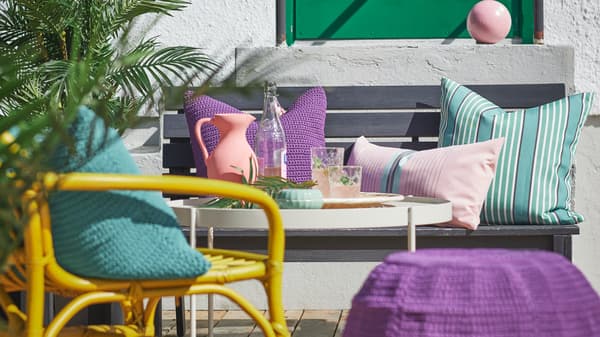 Kényelmes kis sarok az erkélyen természetes anyagokból készült székekkel, lábtartóval és színes párnákkal. 