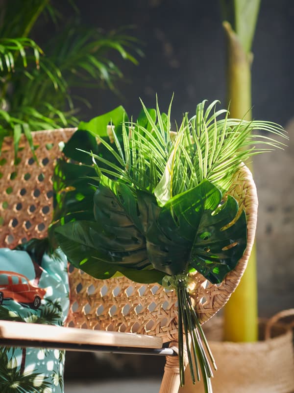 Kerusi ayun rotan anyaman tangan GRÖNADAL dihias dengan daun-daun tiruan SMYCKA yang diikat bersama.