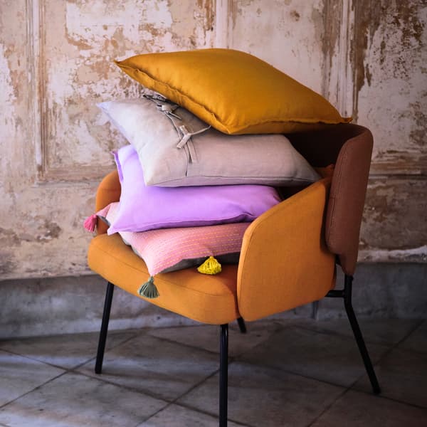 Kerusi berwarna buah labu ditindan dengan pelbagai bantal hiasan berwarna ungu, merah jambu dan kelabu, terletak berlatarbelakangkan dinding berwarna kuning air ala desa.