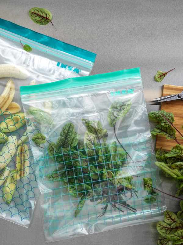 Két különböző méretű ISTAD újrazárható műanyag zacskó, az egyik apróra vágott banánnal, a másik friss céklalevelekkel töltve.