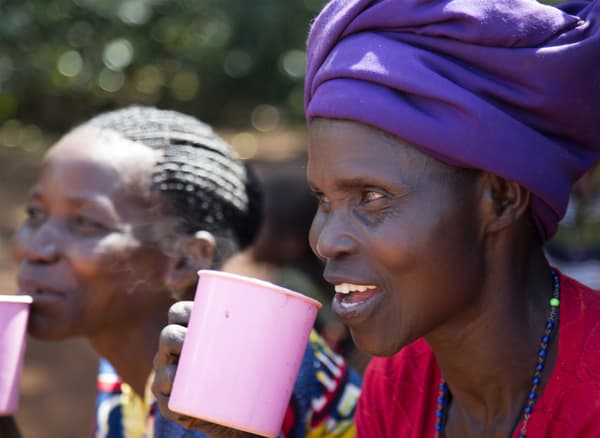 Két nő, színes ruhákban, rózsaszín bögrékből kávéznak.