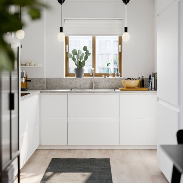 Keuken met witte kastfronten, een licht houten vloer en een betongrijs werkblad. Een raam boven de gootsteen laat natuurlijk licht binnen. 