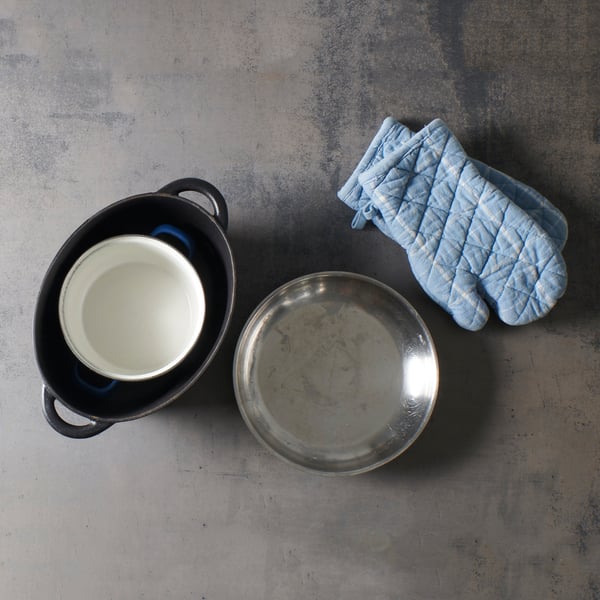 Keukengerei zoals een pan, een schaal en ovenwanten ligt klaar als voorbereiding voor een warmwaterbad dat perfect past bij een IKEA‑achtige DIY‑opstelling.